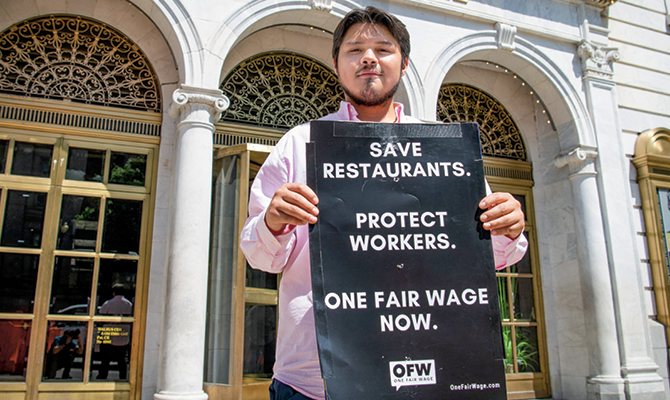 Enlargeable photo of a man with a sign stating: Save Restaurants. Protect Workers. One Fair Wage Now