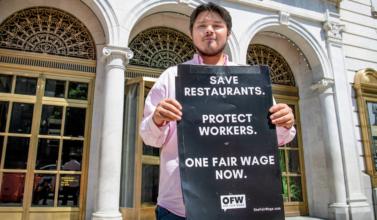 A man with a sign stating: Save Restaurants. Protect Workers. One Fair Wage Now