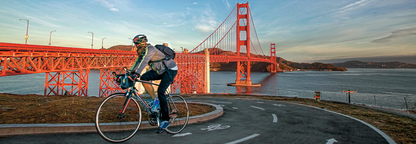 A cyclist in San Francisco riding on designated bike lanes with a red bridge in the background