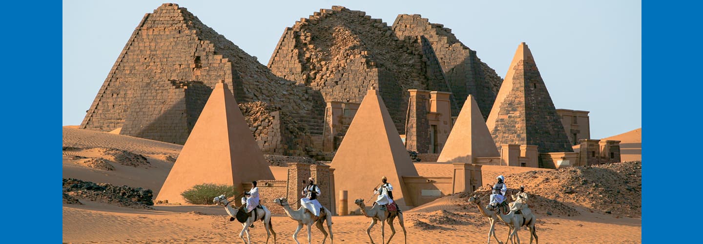 Five men on camels passing the pyramids in Egypt