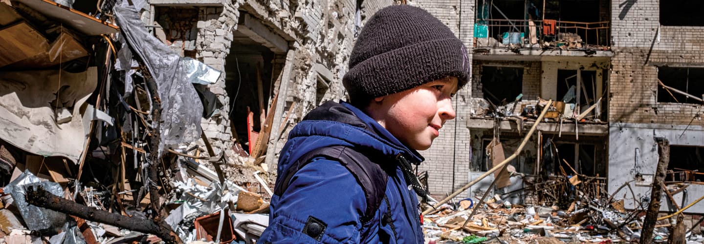 Image of a kid walking on a street with destroyed buildings in background