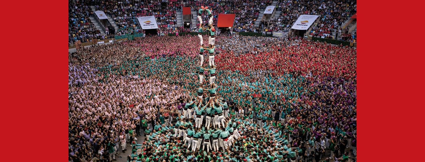 Image of people climbing on top one another to build a tower in front of a large audience