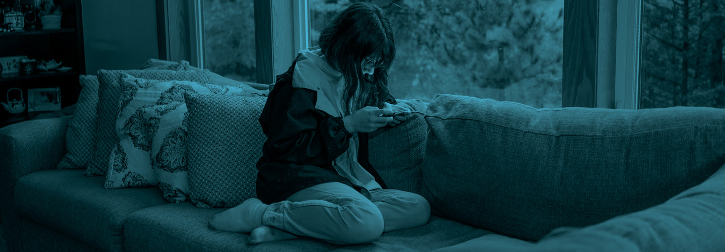 Blue hue photo of a teenager using a phone while sitting on a couch