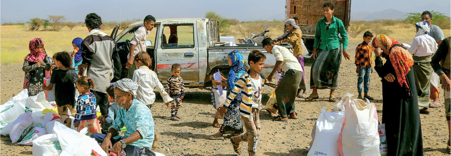 Photo of group of refugees gathered by a car and standing with bags of their items
