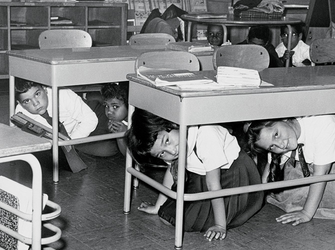 Black & white photo of students hiding under their desks