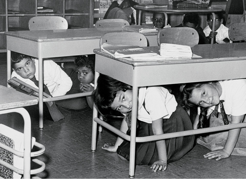 Black & white photo of students hiding under their desks
