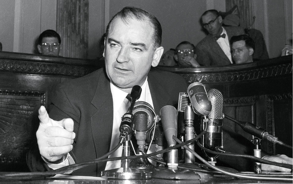 Black & white photo of Joseph McCarthy speaking in front of microphones