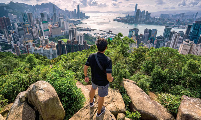 Person standing on a cliff and looking down towards the city below