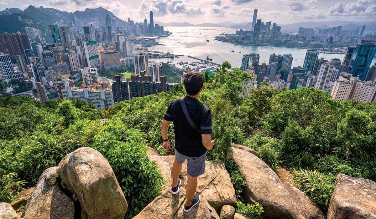 Person standing on a cliff and looking down towards the city below