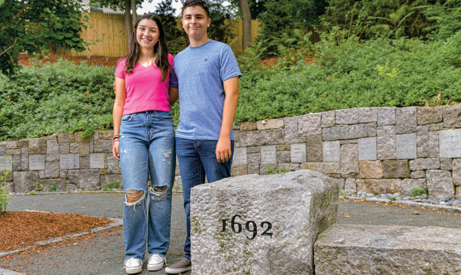 Enlargeable photo of two people posing in front of a stone from 1692 in Salem, MA