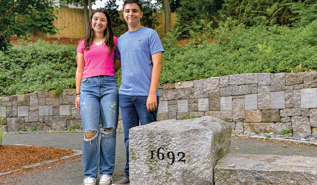 Photo of two people posing in front of a stone from 1692 in Salem, MA