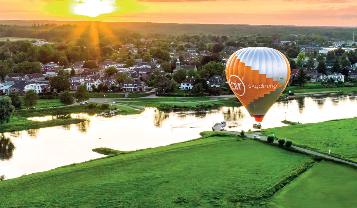 Bird's eye view of a town, river, and hot air balloon all during sunset