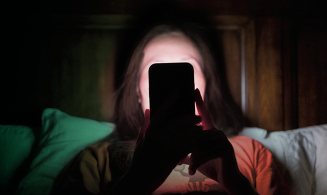 Photo of a person using their phone at night and face is lit up by light of the screen