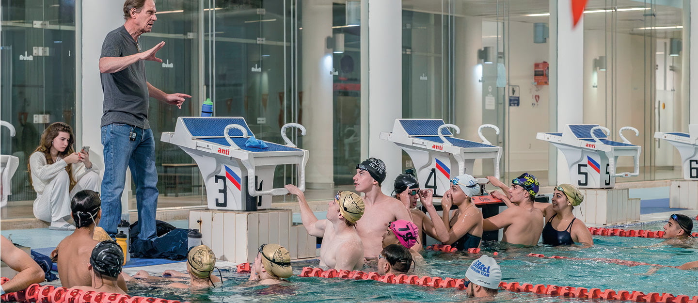 Photo of swimmers in a pool and listening to their coach