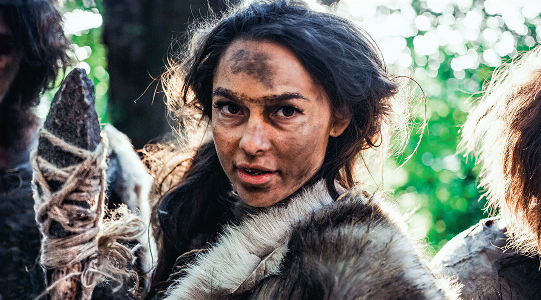 Photo of a cave woman with dirt on her face and holding a weapon