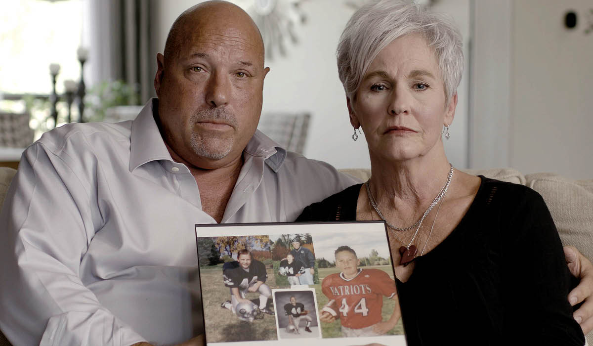 a couple holds up a photo of their son, a football player