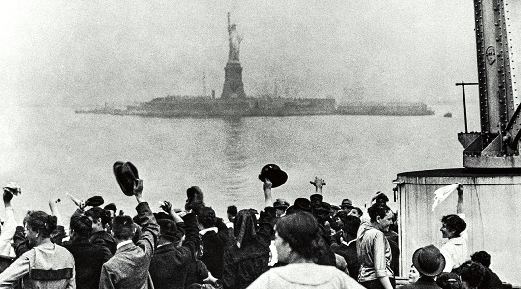 Historical photo of immigrants on a ship approaching the Statue of Liberty