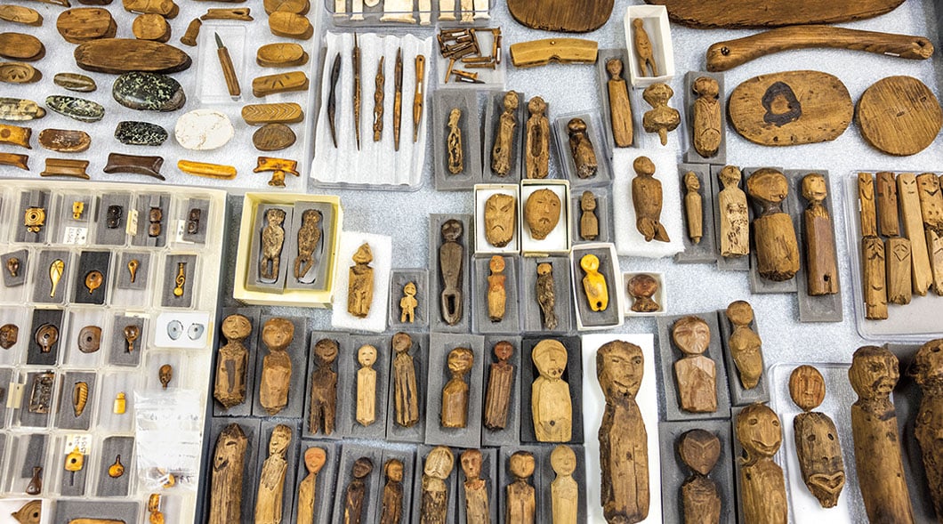 A large collection of carved wooden figurines, tools, and small artifacts arranged on a flat surface