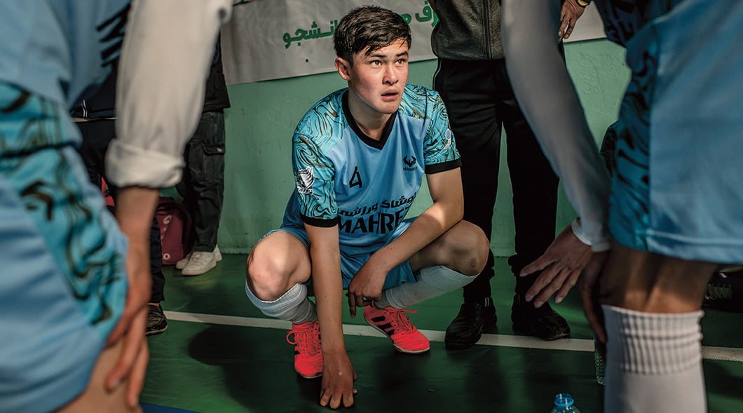 A soccer player in a Mahre jersey crouches on a court, surrounded by teammates